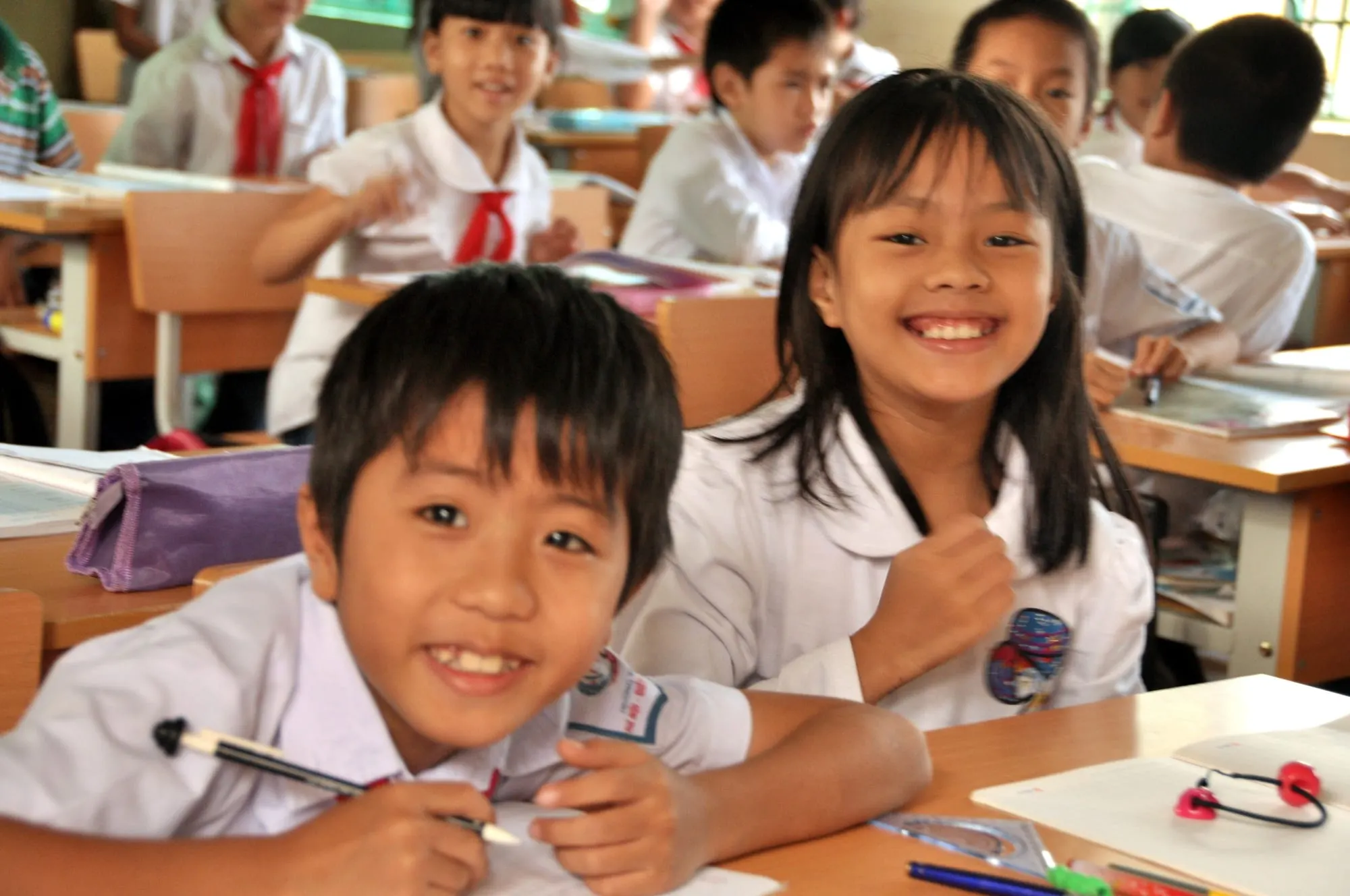 Học sinh tiểu học mỉm cười bên bàn học trong lớp