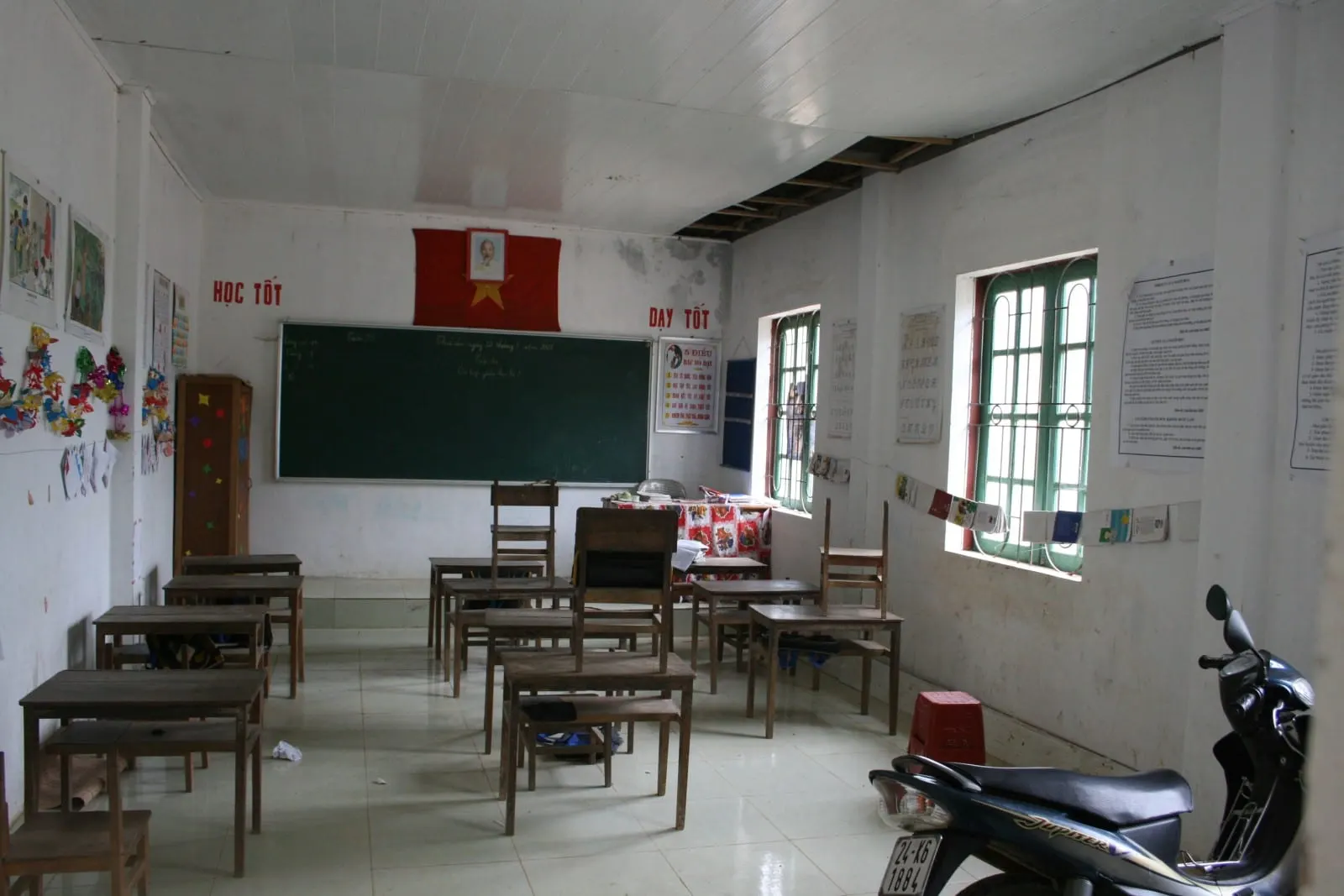 Phòng học đơn sơ ở một trường làng với bàn ghế gỗ và bảng đen